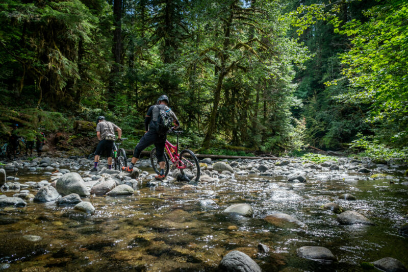 Mountain bikers cross a creek while on a mountain bike adventure in the Old Cascade Crest. 