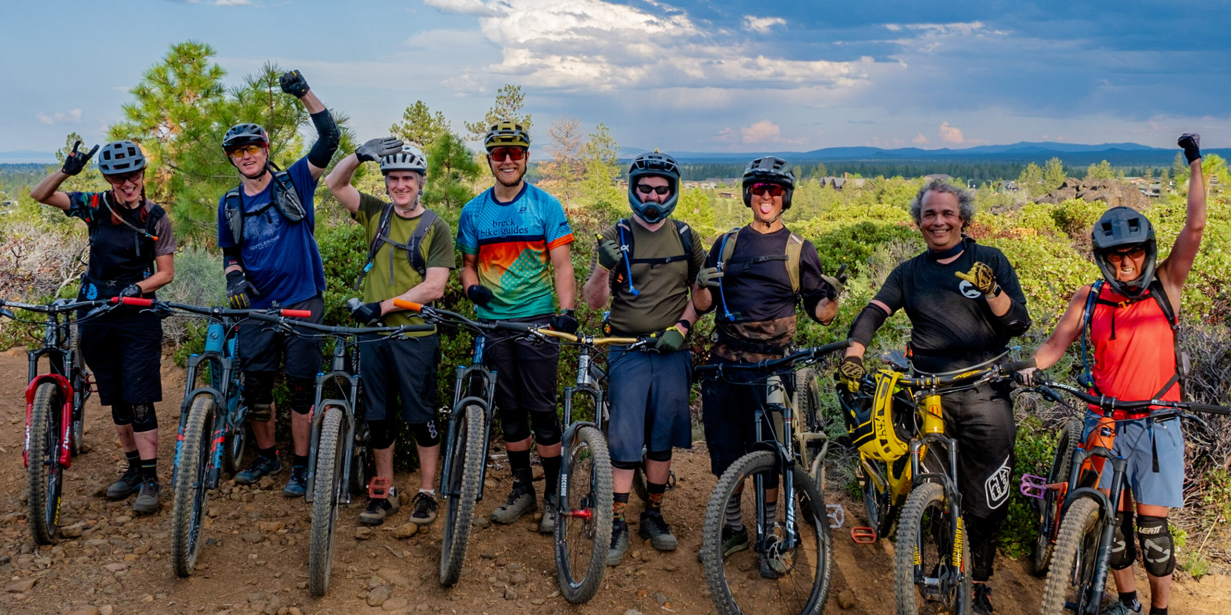 A class of mountain bikers poses for a group picture with a the cloudy sky in the background.